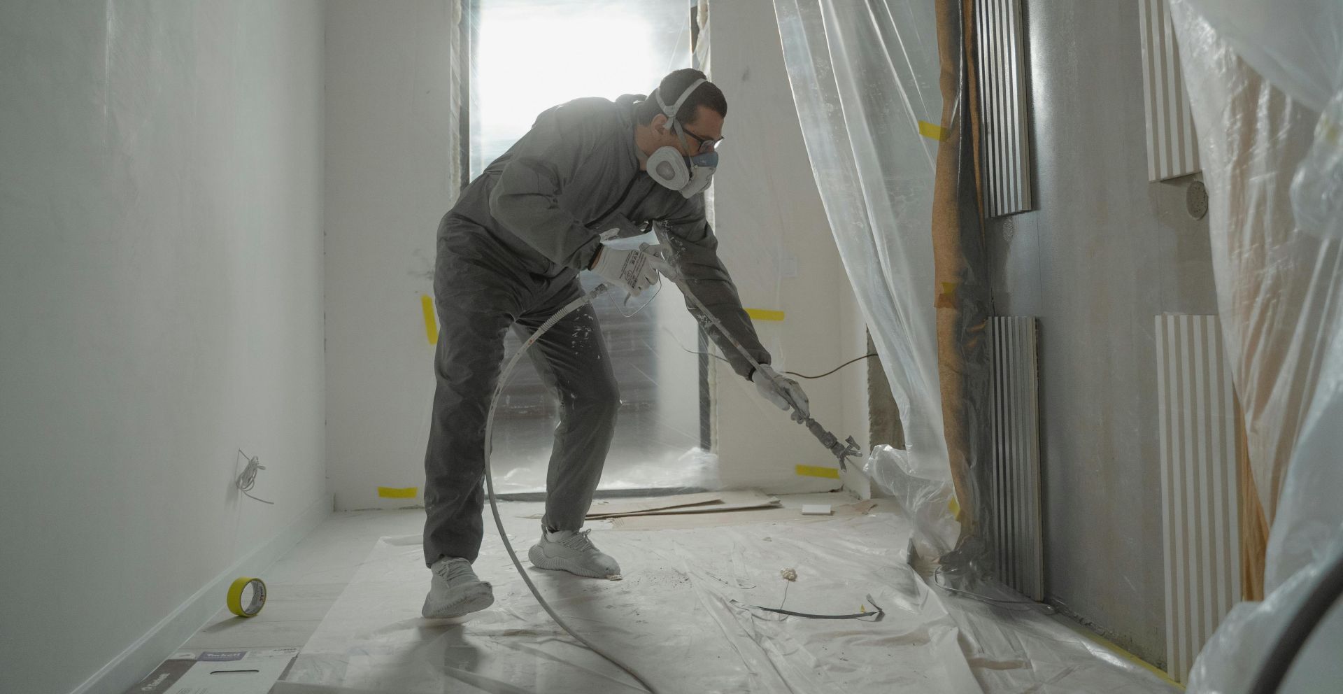 A worker in protective gear painting walls during an indoor renovation project.