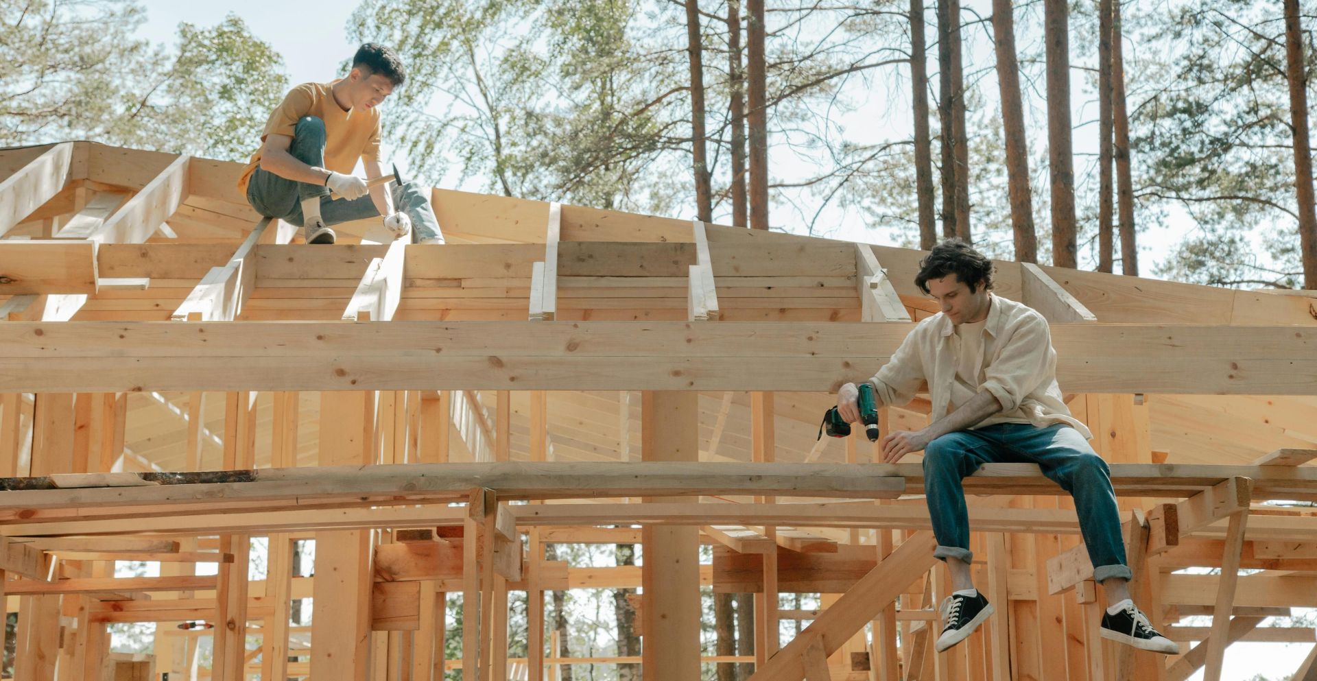 Two male carpenters working on a wooden framework of a house under bright daylight.